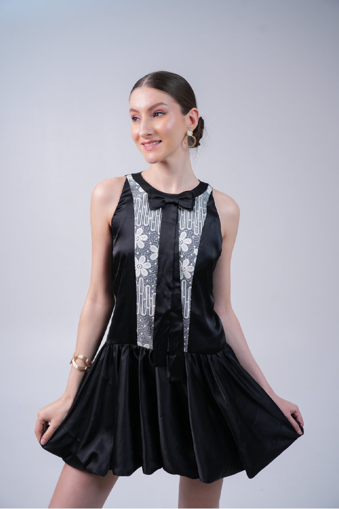 Woman wearing a black mini dress with white lace details on a gray background